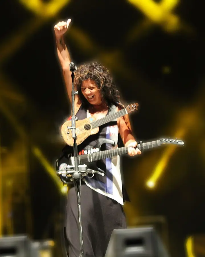 Rosana en el escenario, sonriendo, con el brazo en alto y dos guitarras colgadas.